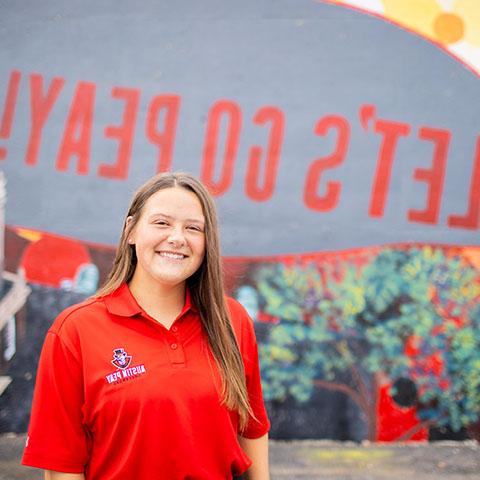Math education student, Alex Edwards stands in front of mural.
